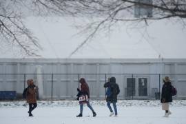 Varias personas caminan por un campo deportivo nevado frente a un albergue para migrantes en la Isla Randall de Nueva York.