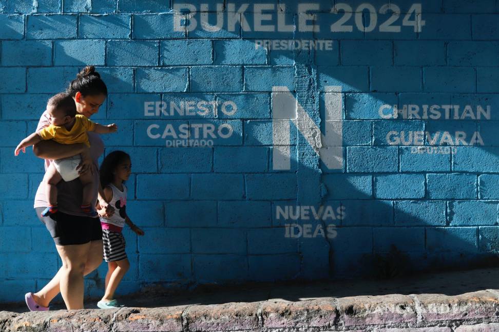 $!Una mujer camina con sus hijos junto a un mural que promociona al presidente Nayib Bukele, que se postula para la reelección en San Salvador, El Salvador.