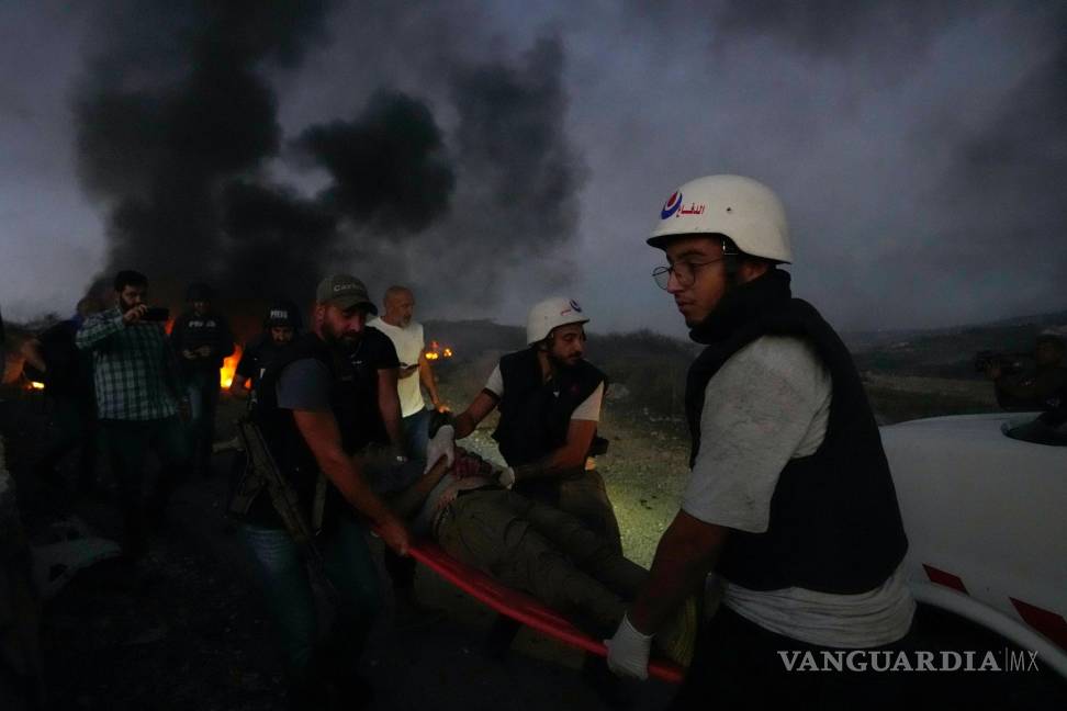 $!Trabajadores de protección civil y un agente de seguridad libanés cargan a un periodista que resultó herido por la caída de un proyectil israelí en Alma al-Shaab.