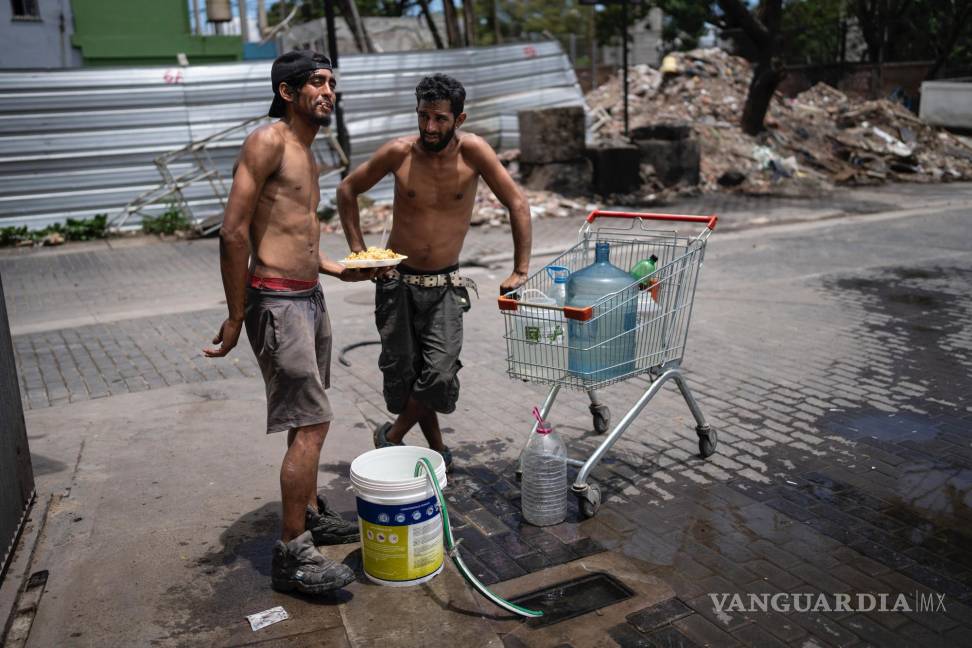 $!Nicolás Gonzáles (i) y Maxi Suárez rellenan recipientes de agua después de retirar un plato de comida de la Casa Comunitaria del Fondo.