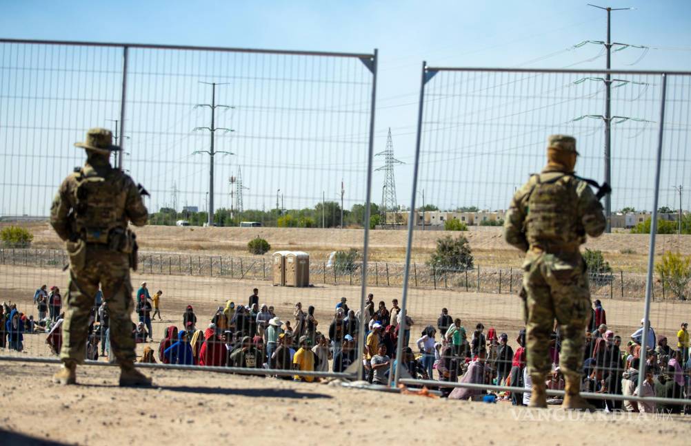 $!Migrantes esperan en fila junto a la valla fronteriza bajo la vigilancia de la Guardia Nacional de Texas para ingresar a El Paso, Texas.