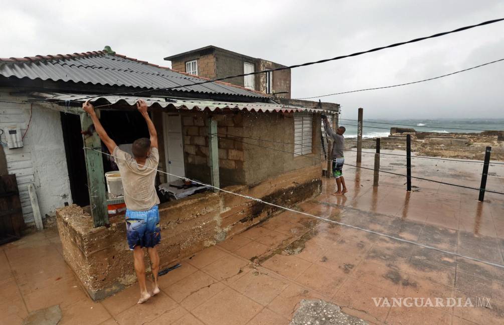 $!Personas amarran las tejas del techo de una casa debido al paso del huracán Rafael en La Habana, Cuba.