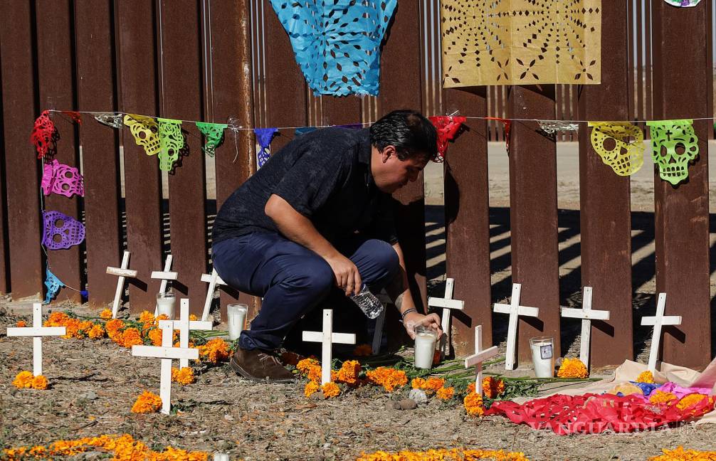 $!Un activista coloca una veladora en una ofrenda de Día de Muertos hoy, junto al muro fronterizo en Playas de Tijuana (México).