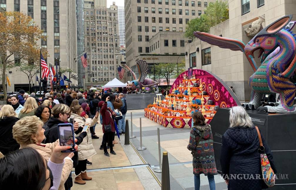 $!Decenas de personas toman fotos al enorme altar del Día de los Muertos, decorado con pétalos de vibrantes colores, calaveras, velas, botellas de tequila, vasijas y perros de la raza xoloitzcuintle, instalado en una de las plazas del Rockefeller Center en Nueva York. EFE/Helen Cook