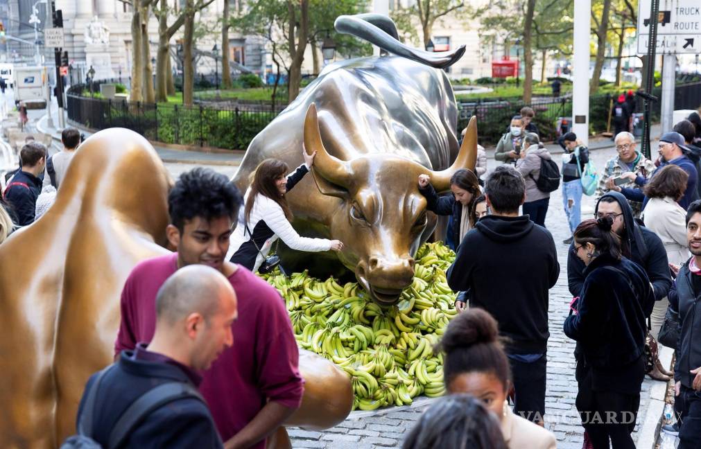 $!La gente mira la estatua de “Charging Bull” en Broadway rodeada de plátanos y una estatua de un gorila como una instalación de protesta organizada por Sapien. EFE/EPA/Justin Lane