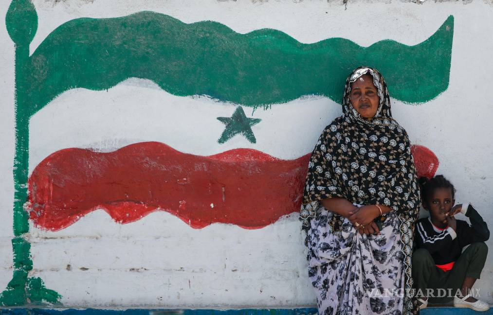 $!Una mujer y un niño descansan en un muro que la bandera de Somalilania, en Hargeisa, Somalilandia, un territorio semiautónomo.