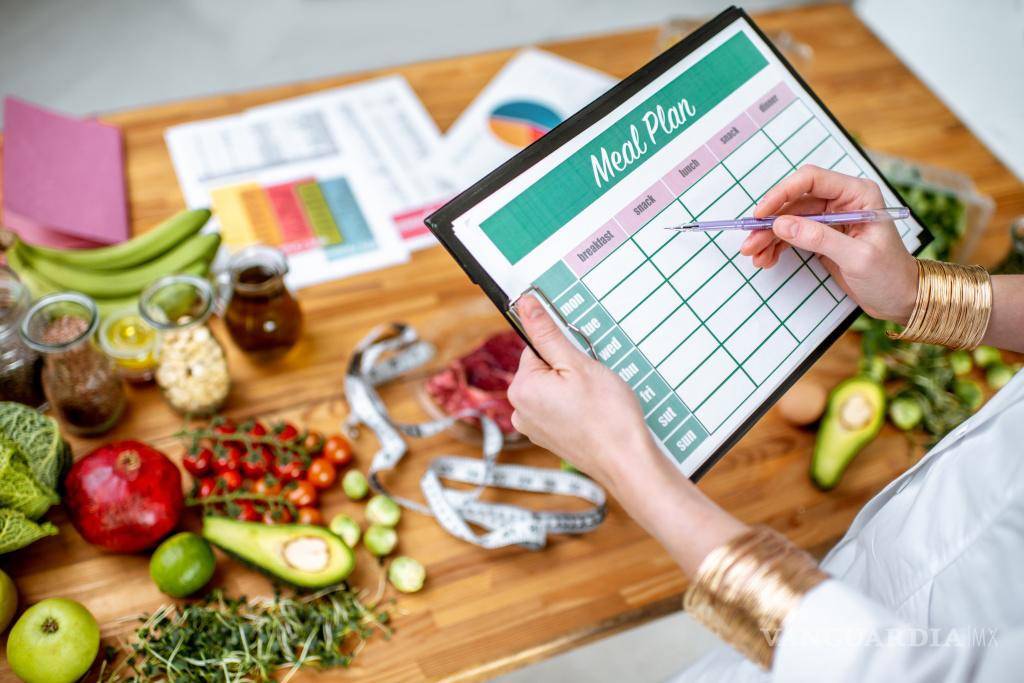 $!Nutricionista escribiendo un plan dietético semanal junto a algunos alimentos.