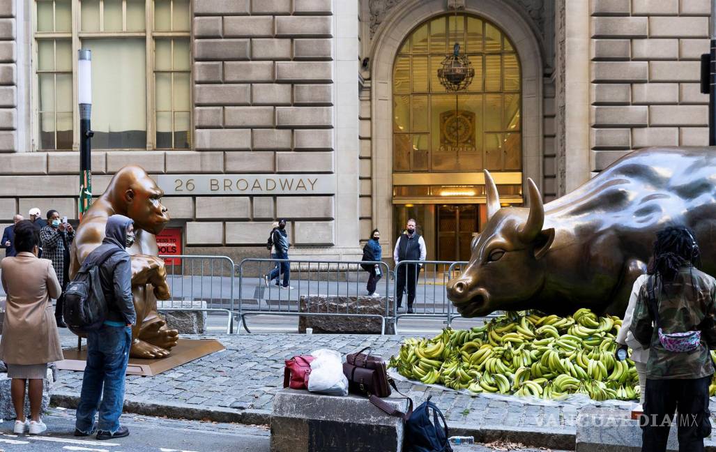 $!La gente mira la estatua de “Charging Bull” en Broadway rodeada de plátanos y una estatua de un gorila como una instalación de protesta organizada por Sapien. EFE/EPA/Justin Lane