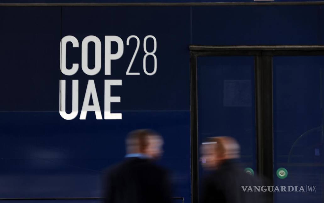 $!Dos personas frente a un autobús con el logotipo de la COP28 antes de la Conferencia de las Naciones Unidas sobre el Cambio Climático en Dubai.