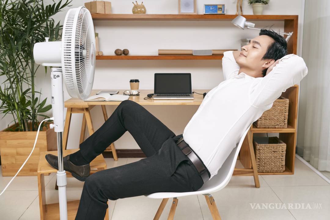 $!Young Asian office worker resting on chair in front of ventilator and refreshing from heat at office