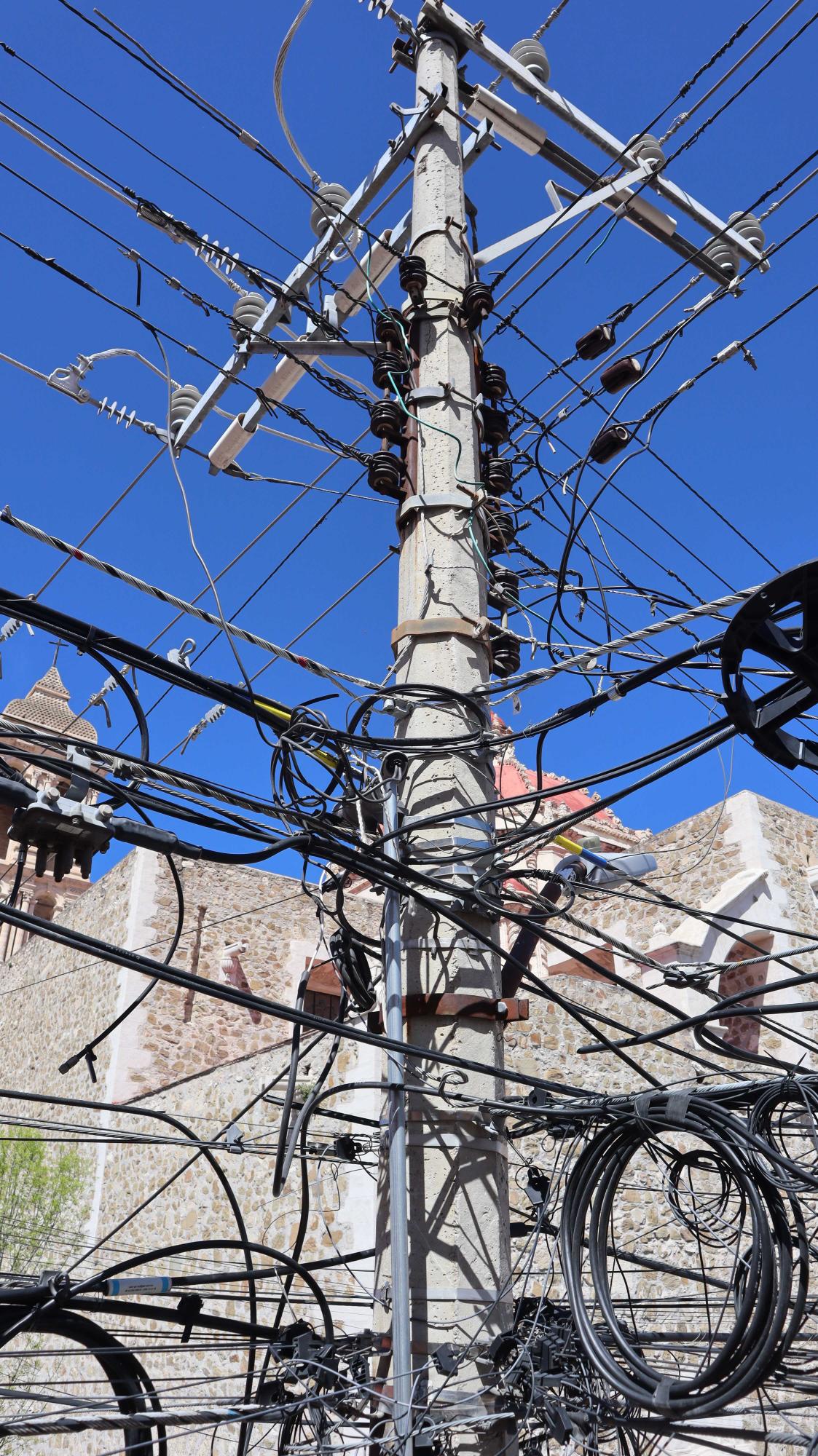 $!En la esquina de las calles Juárez y Bravo una gigantesca “telaraña” de cables pende de los postes, con el riesgo de caer sobre los transeúntes.