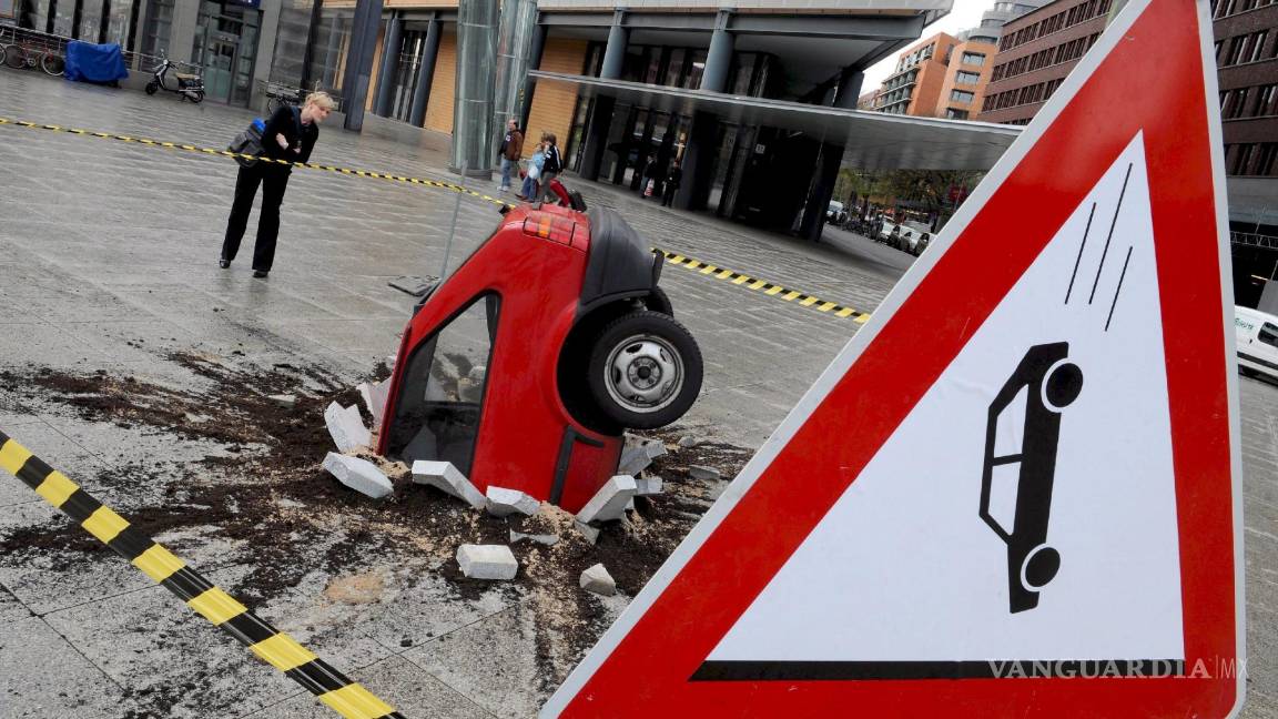 $!Unos peatones observan una escultura de un vehículo estrellado en la Postdam Square de Berlín. Los vídeos falsos cada vez abundan más.