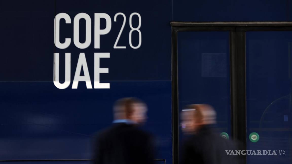 $!Dos personas frente a un autobús con el logotipo de la COP28 antes de la Conferencia de las Naciones Unidas sobre el Cambio Climático en Dubai.
