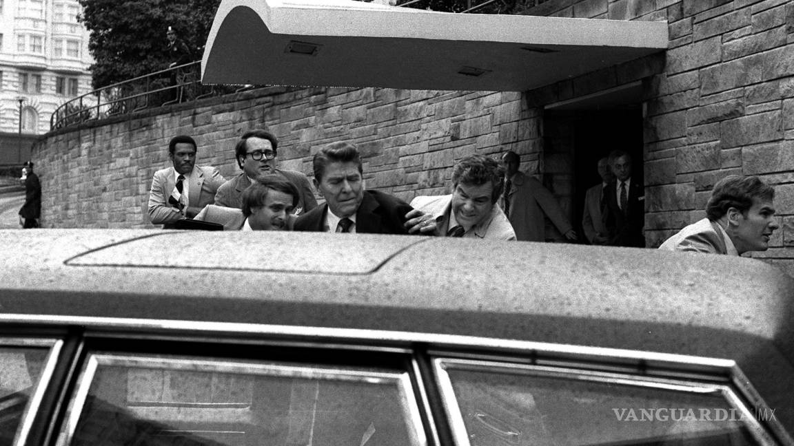 $!El presidente Ronald Reagan (c) es empujado a la limusina del presidente por agentes del servicio secreto después de recibir un disparo en Washington.