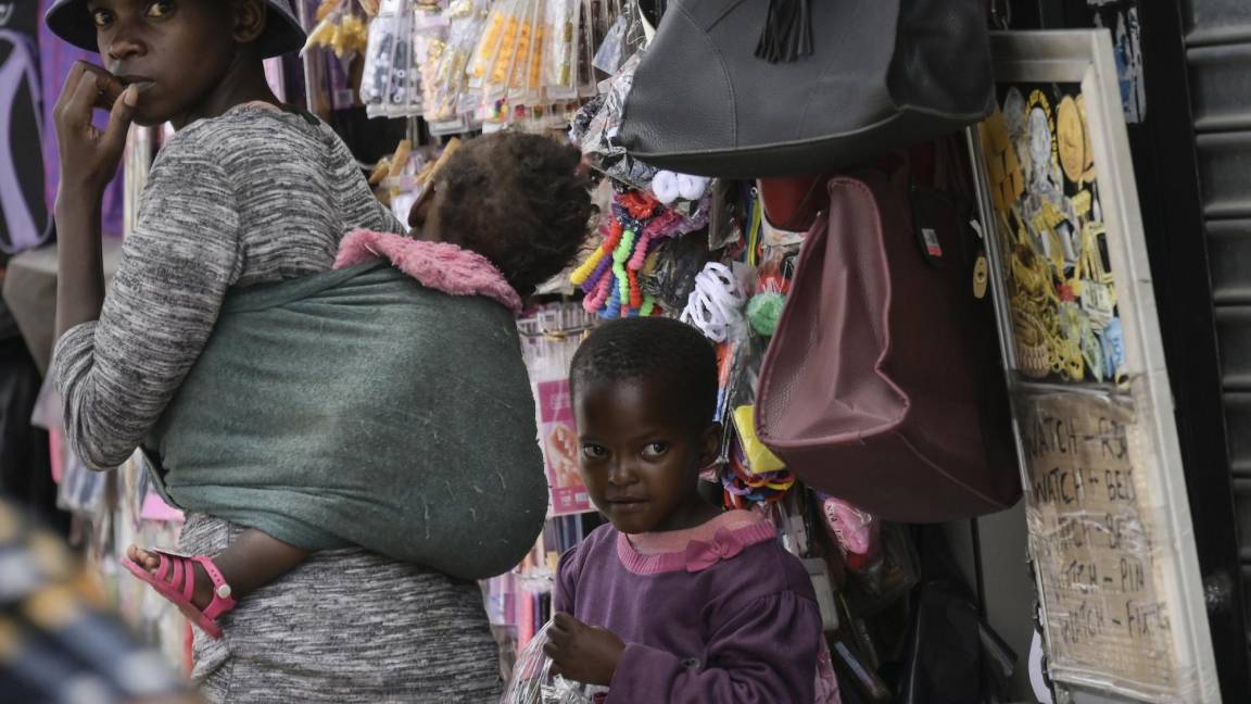 $!Una mujer sin máscara con dos niños camina por la concurrida parada de taxis de Bara en Soweto, Sudáfrica.