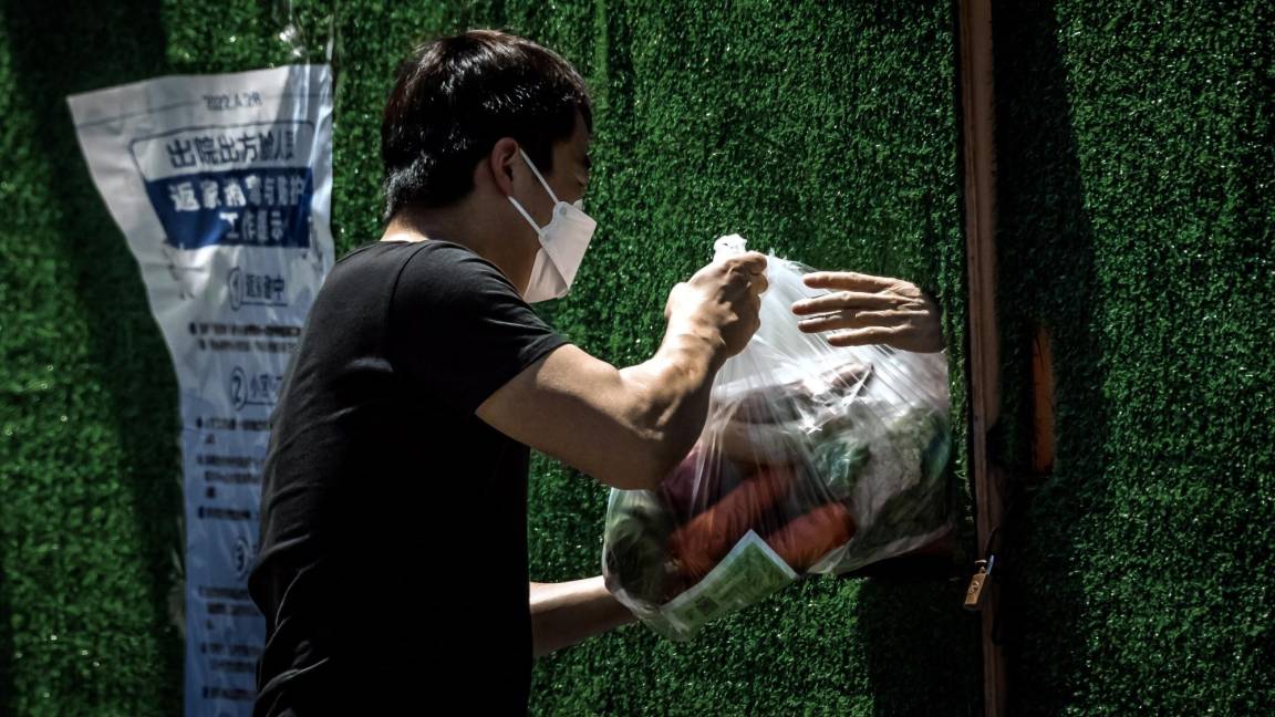 $!Un repartidor pasa comida a la persona en cuarentena a través del agujero en la cerca en medio del bloqueo de Covid-19 en curso en Shanghái, China.