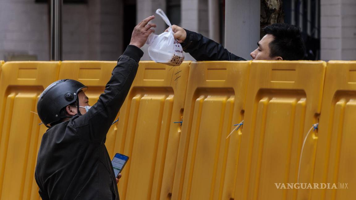 $!Un hombre entrega comida a un hombre en el complejo en cuarentena en medio del cierre, en el lado de Puxi de la ciudad, en Shanghái, China.
