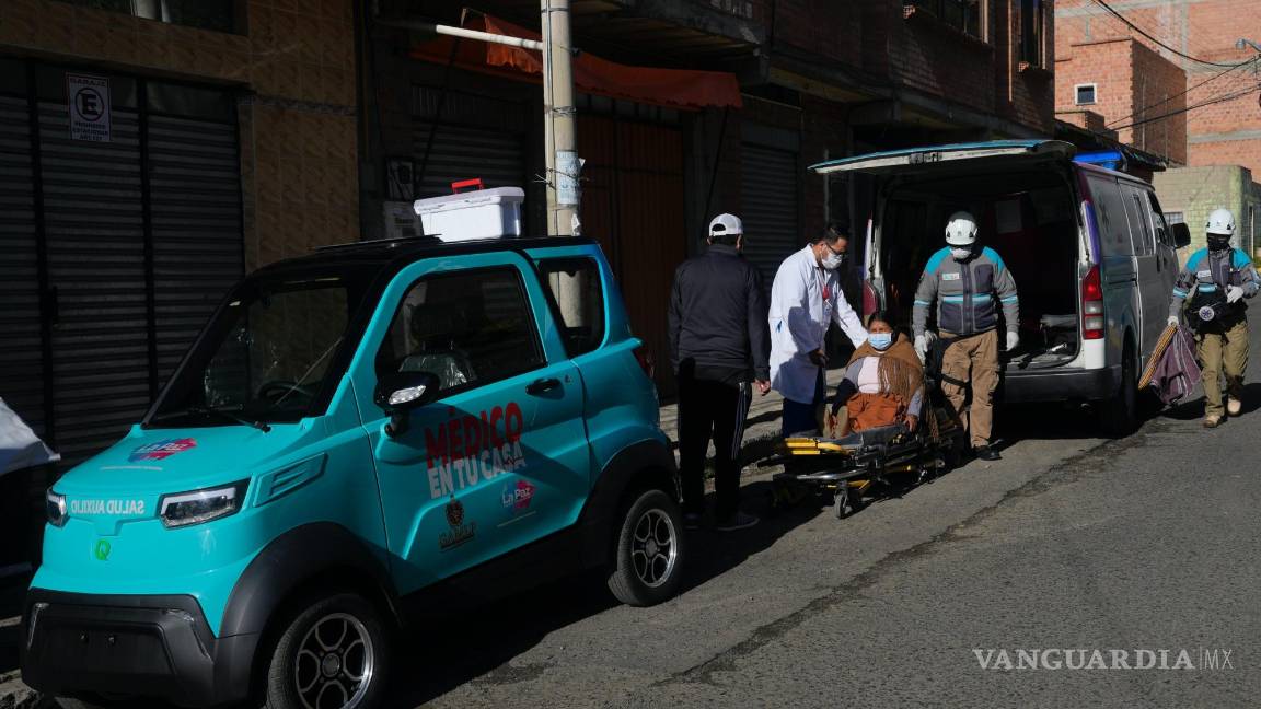 $!El Dr. Carlos Ortuno atiende a Juana Velasco flanqueado por un auto eléctrico Quantum de fabricación boliviana y una ambulancia, en La Paz, Bolivia.