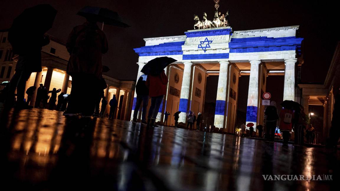 $!Personas observan la Puerta de Brandenburgo se ilumina con los colores de la bandera israelí como muestra de solidaridad, en Berlín, Alemania.