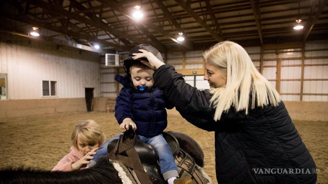 $!Louann Gross (i), y Tammy Cunningham (d) ayudan al hijo de Tammy, Calum, a subirse a un caballo en una granja y guardería en Kokomo, Indiana.