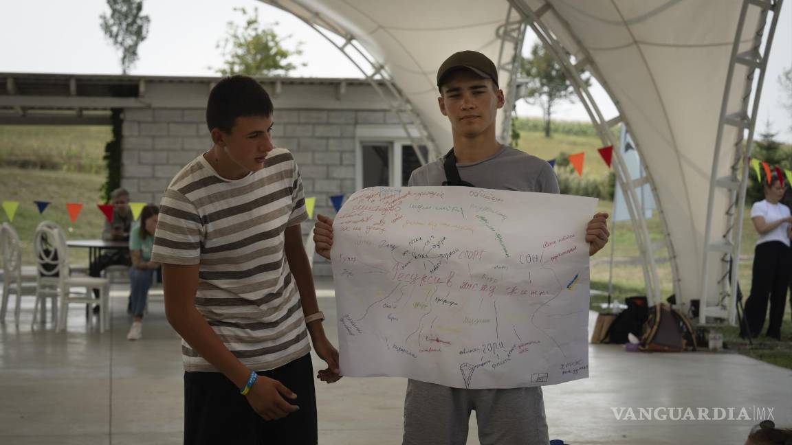 $!Oleksandr Hryshchenko (I) observa a Valerii Soldatenko, de 16 años, mostrar una pancarta que dice “recursos de vida” en el campamento de rehabilitación