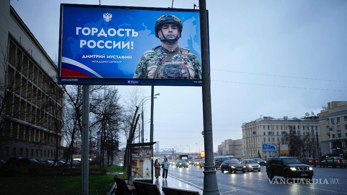 $!Dos mujeres están paradas en una parada de autobús con un cartel que dice “Orgullo de Rusia” de un soldado ruso en Moscú, Rusia.
