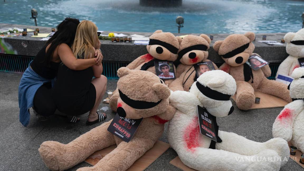 $!Dos mujeres se abrazan junto a una instalación de ositos de peluche gigantes con los ojos vendados con fotografías de israelíes cautivos en Gaza, en Tel Aviv, Israel.