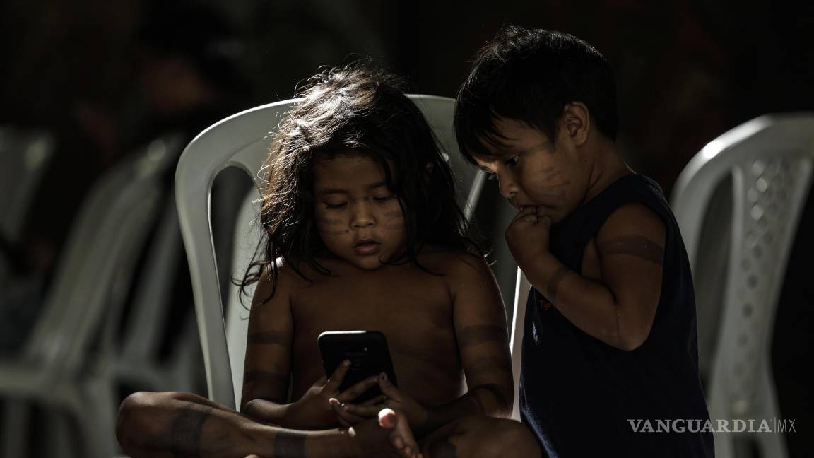 $!Una niña y un niño indígena miran un teléfono en el Parque de Igarapé en la ciudad de Belém, estado de Pará (Brasil).