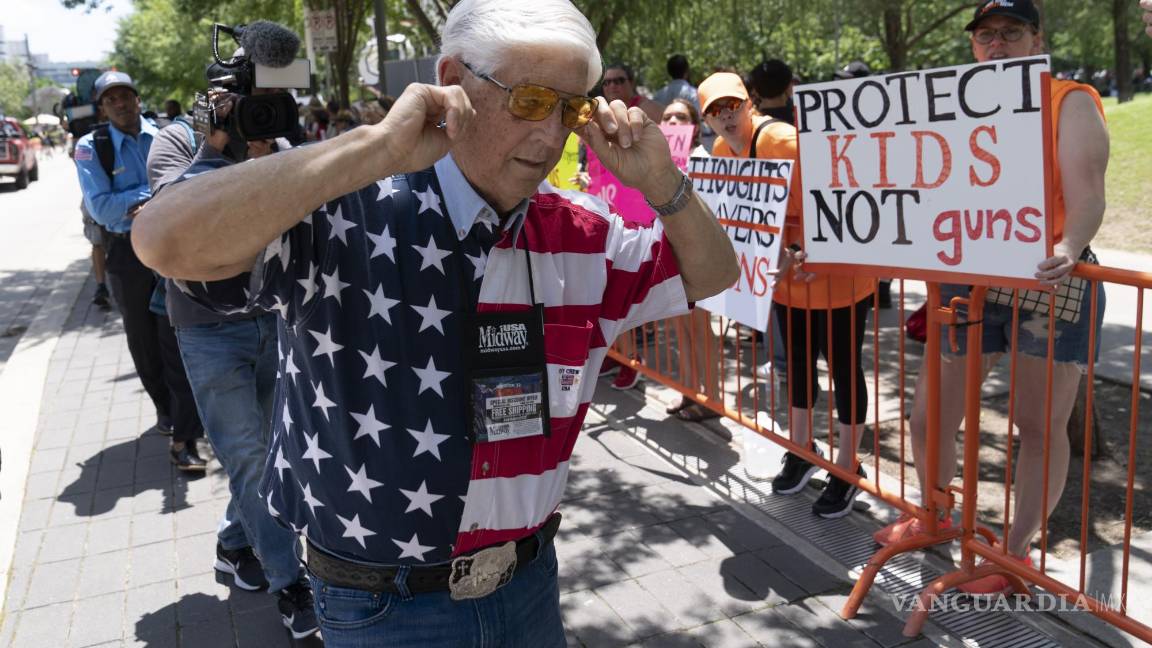 $!Un miembro de la Asociación Nacional del Rifle se tapa los oídos mientras camina junto a manifestantes durante la reunión anual de la NRA en Houston.