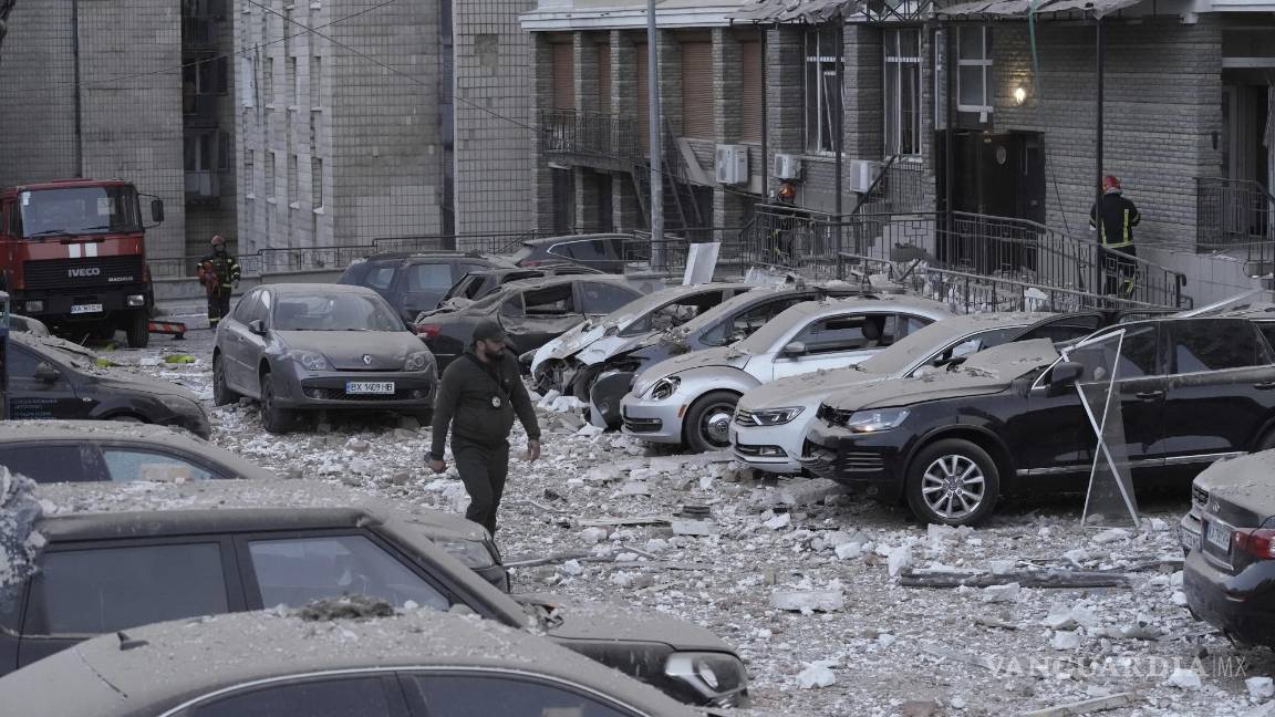 $!Un agente de policía camina por un estacionamiento con autos dañados, frente a un edificio de varias plantas, luego de un ataque ruso sobre Kiev.