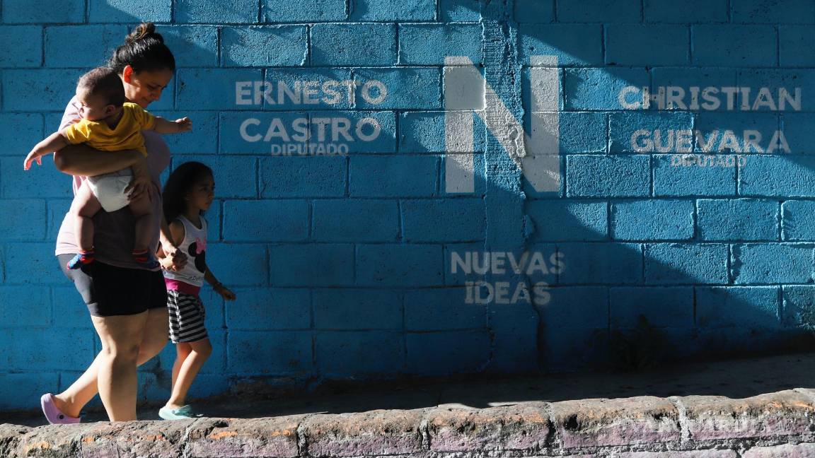 $!Una mujer camina con sus hijos junto a un mural que promociona al presidente Nayib Bukele, que se postula para la reelección en San Salvador, El Salvador.