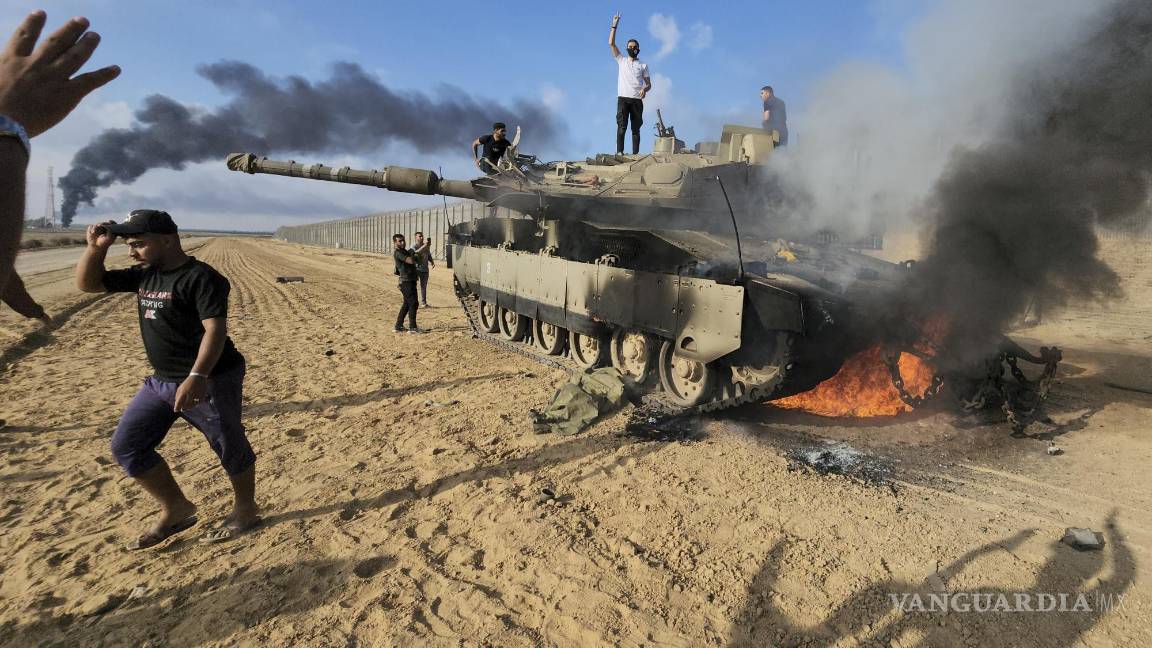 $!Palestinos celebran junto a un tanque israelí destruido en la cerca fronteriza de la Franja de Gaza, al este de Jan Yunis, en el sur del enclave, el 7 de octubre de 2023.