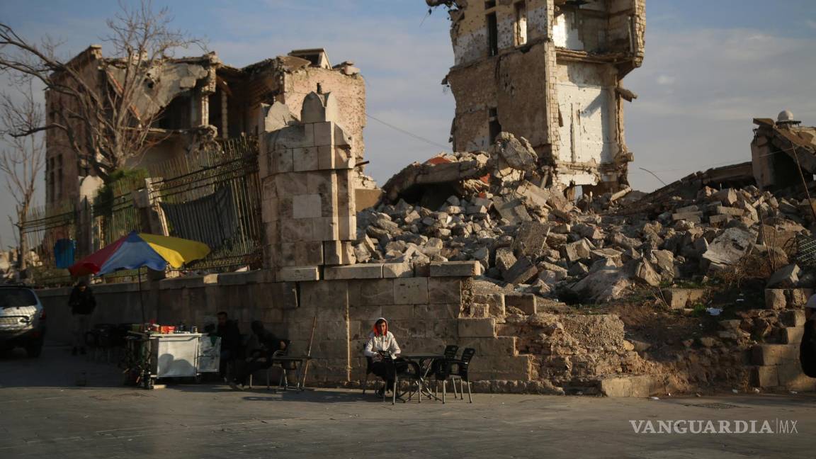 $!Un vendedor ambulante u un edificio dañado mientras la gente se reúne en el lado de la Ciudadela de Alepo después de que la oposición tomó el control de la ciudad.