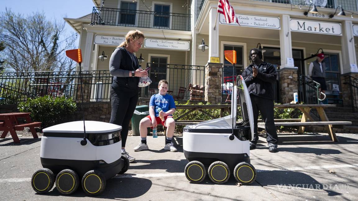 $!30 de marzo de 2020. Personas reciben comida de robots de reparto de alimentos, famosos durante la pandemia, en el mercado Broad Branch Market en Washington.