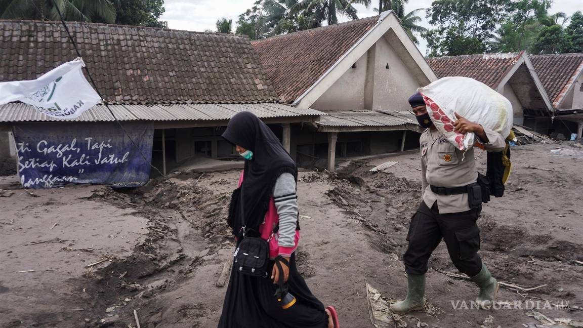 $!Un oficial de policía lleva un saco mientras ayuda a un aldeano a buscar víctimas en una aldea enterrada en cenizas volcánicas de la erupción del monte Semeru.EFE/EPA/AMMAR