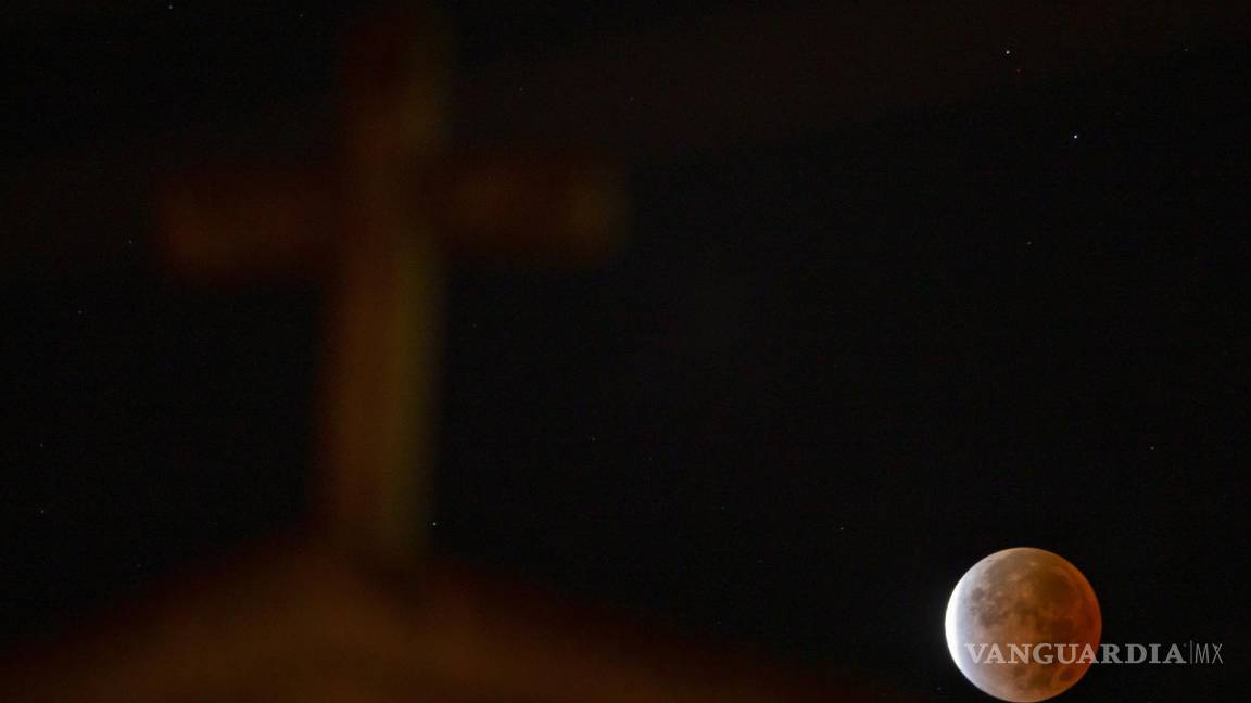 $!Una vista del eclipse lunar detrás de la iglesia de St. Williams en Cincinnati. El eclipse fue el más largo de este siglo y más largo que cualquier otro eclipse que se remonta a 580 años. AP/Albert Cesare /The Cincinnati Enquirer