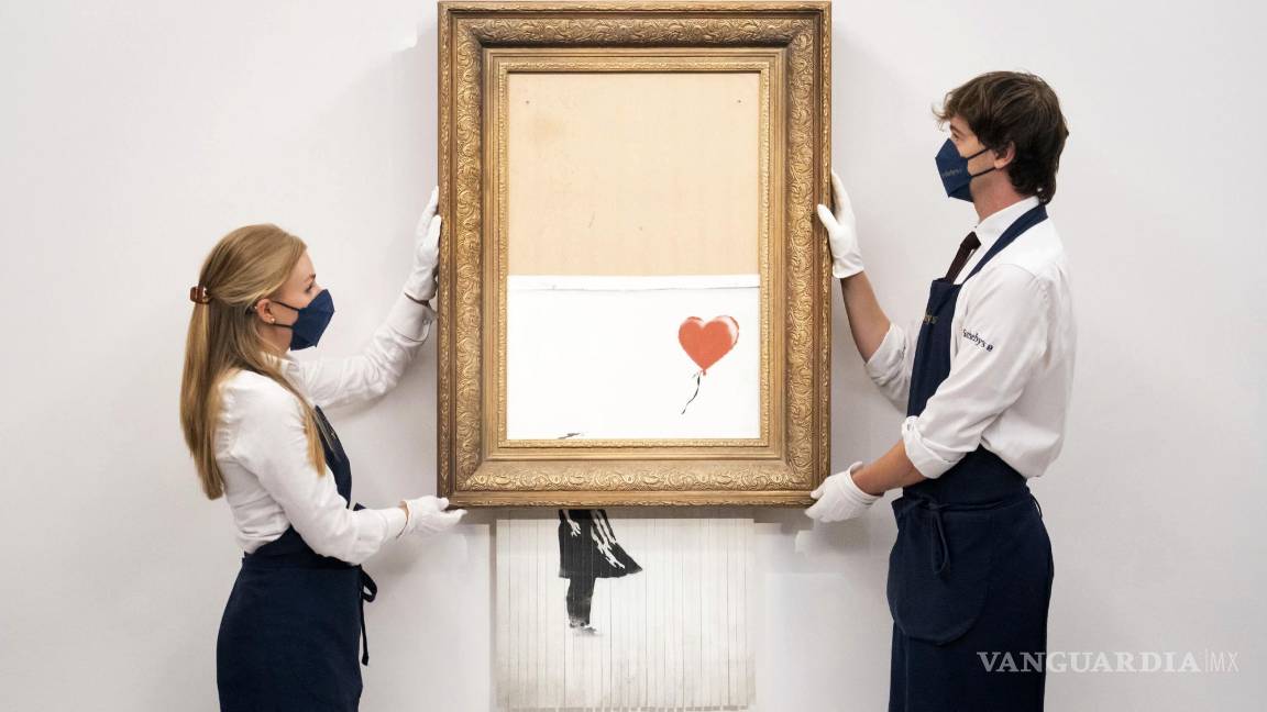 $!En esta foto del 3 de septiembre de 2021, manipuladores de arte sostienen Love is in the Bin de Banksy en la casa de subastas Sotheby's en Londres. AP/Dominic Lipinski/PA