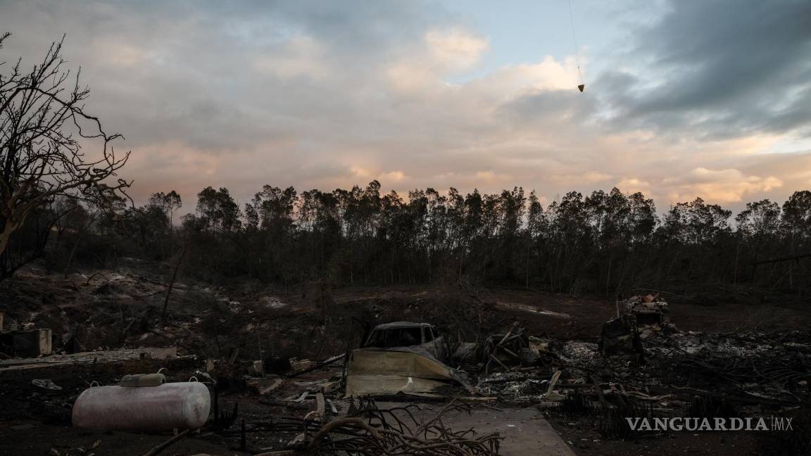 $!Un helicóptero arroja agua sobre puntos calientes cerca de casas quemadas en Kula, Hawái.