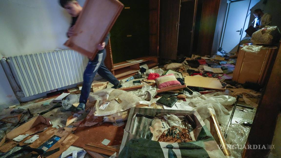 $!Un hombre camina junto a un retrato roto del difunto presidente sirio Hafez Assad. La gente busca pertenencias en la residencia privada saqueada de Bashar Assad.