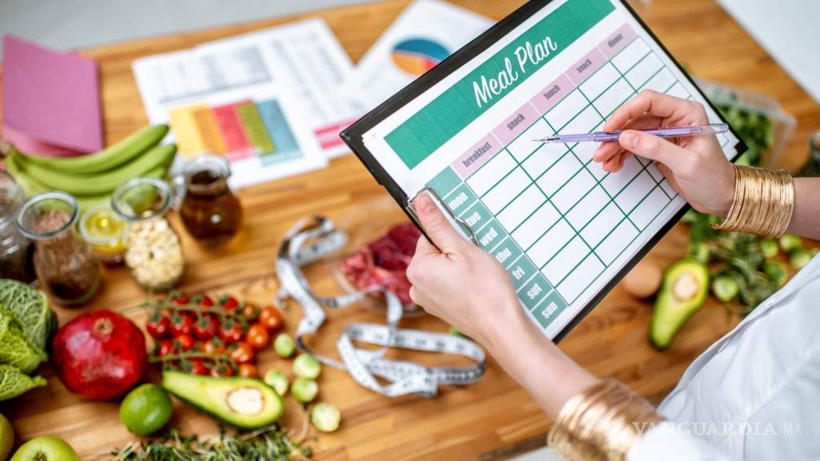 $!Nutricionista escribiendo un plan dietético semanal junto a algunos alimentos.