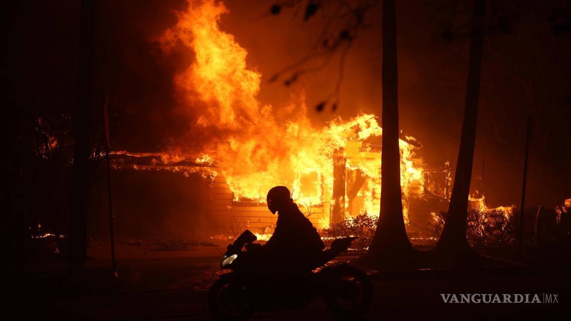 $!Una persona conduce su motocicleta junto a una casa en llamas durante los incendios en Palisades , California, Estados Unidos.