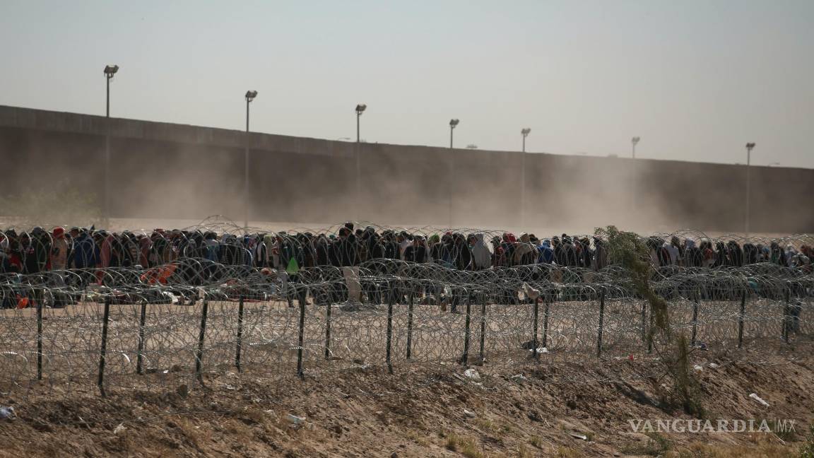 $!Migrantes alineados entre una valla con alambre de púas y el muro fronterizo entre Estados Unidos y México, visto desde Ciudad Juárez, México.