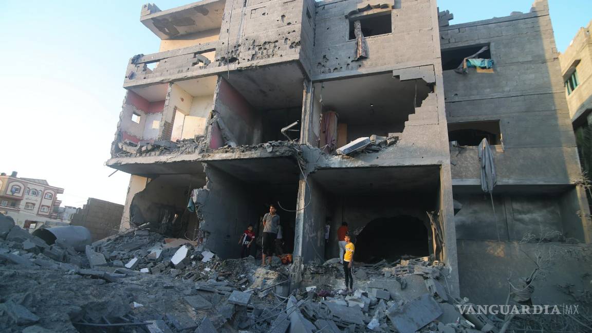 $!Palestinos de pie junto a un edificio destruido en un ataque aéreo israelí en la frontera de Rafah, en la Franja de Gaza, el lunes 16 de octubre de 2023.