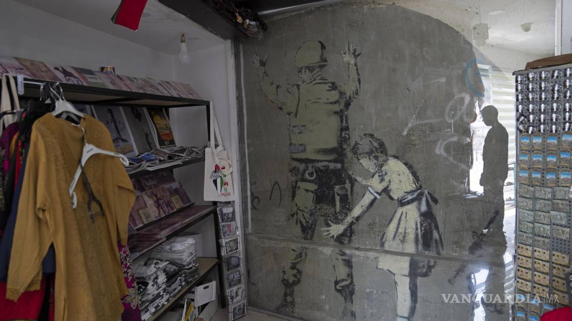 $!Un mural del reservado artista de grafiti británico Banksy está cubierto con vidrio protector dentro de una tienda de regalos, en la ciudad de Belén, Cisjordania.