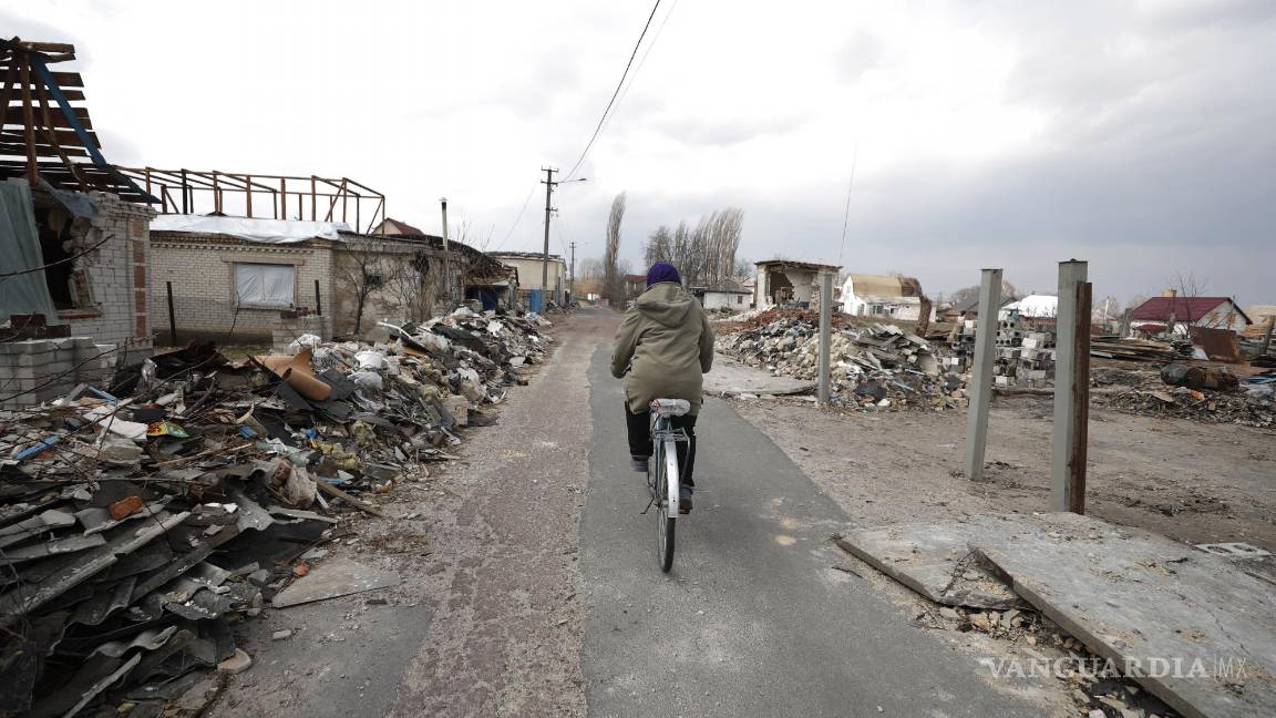 $!Una mujer monta en bicicleta frente a las casas dañadas después de un ataque aéreo ruso en el pueblo de Ulica Szkolna, óblast de Kiev.