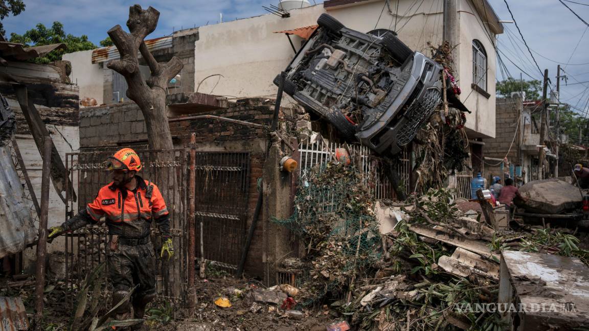 $!Un rescatista, miembro de la brigada de voluntarios Topos, trabaja junto a un automóvil colgado de una cerca junto a una casa dañada en Poza Rica.