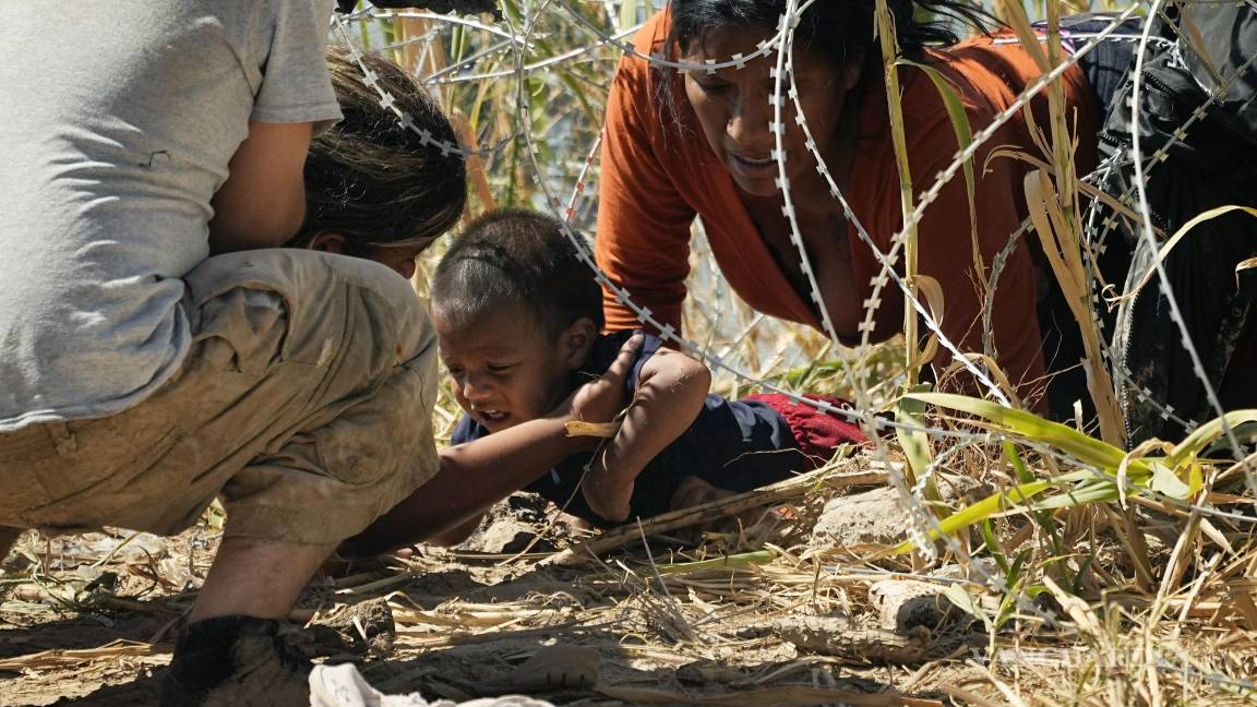 $!Migrantes logran cruzar a un niño por debajo de una alambrada de púas, en la frontera de Eagle Pass y Piedras Negras.