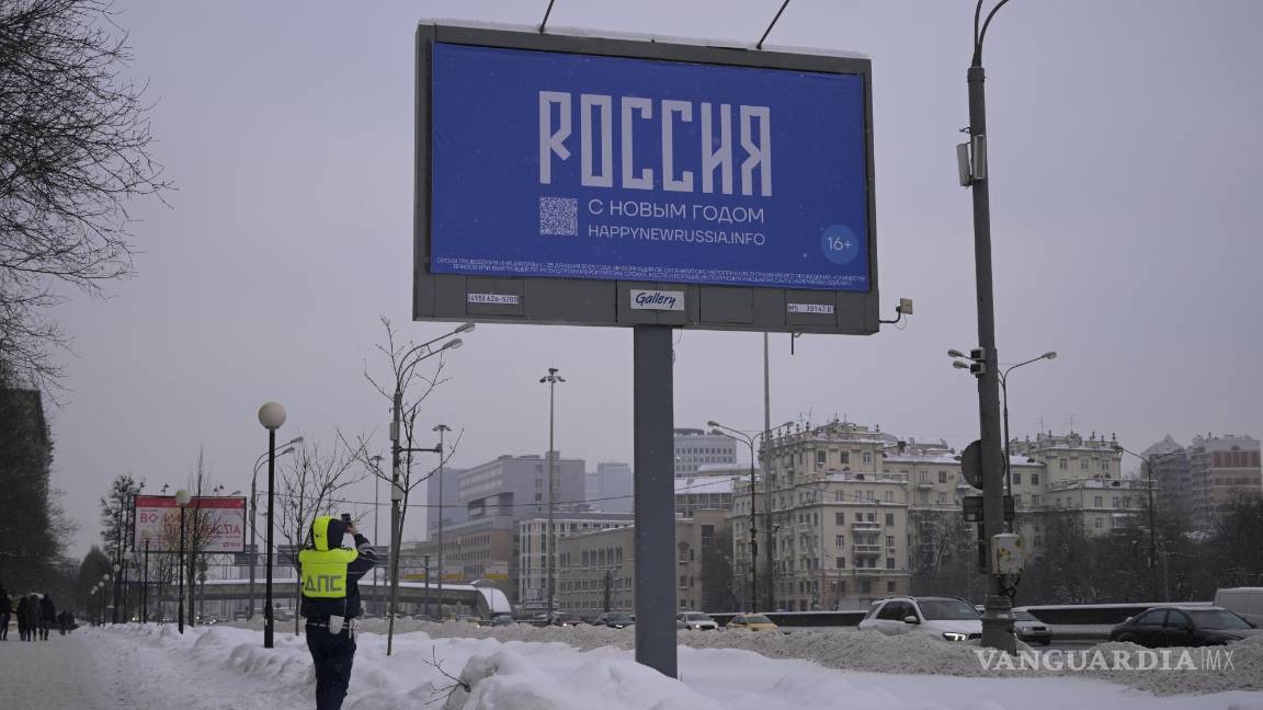 $!Un oficial de la policía de tránsito toma una fotografía de un cartel con las palabras Feliz Año Nuevo y el código QR en Moscú, Rusia.