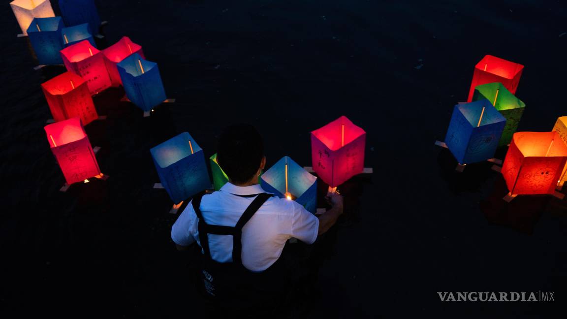 $!Un voluntario coloca linternas de papel que flotan a lo largo del río Motoyasu frente a la Cúpula de la Bomba Atómica en el 80.º aniversario del bombardeo atómico.