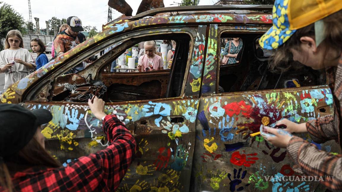 $!Artistas pintan junto a un grupo de niños coches quemados durante los combates entre las tropas ucranianas y rusas, este viernes en Bucha, Ucrania.